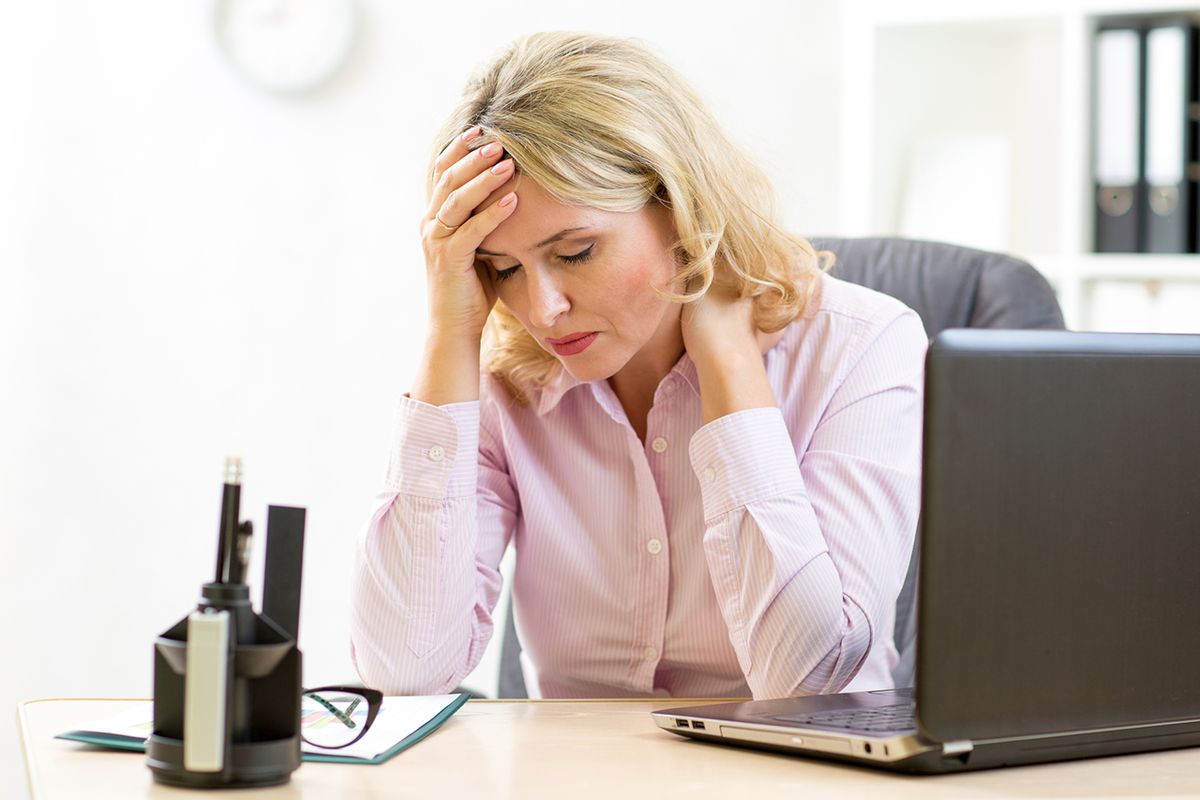 A frustrated woman holding her head while waiting at a laptop